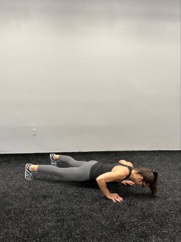 Woman in the bottom of a push up. Hands under shoulders, straight body, elbows bending about 45 degrees away from the body.