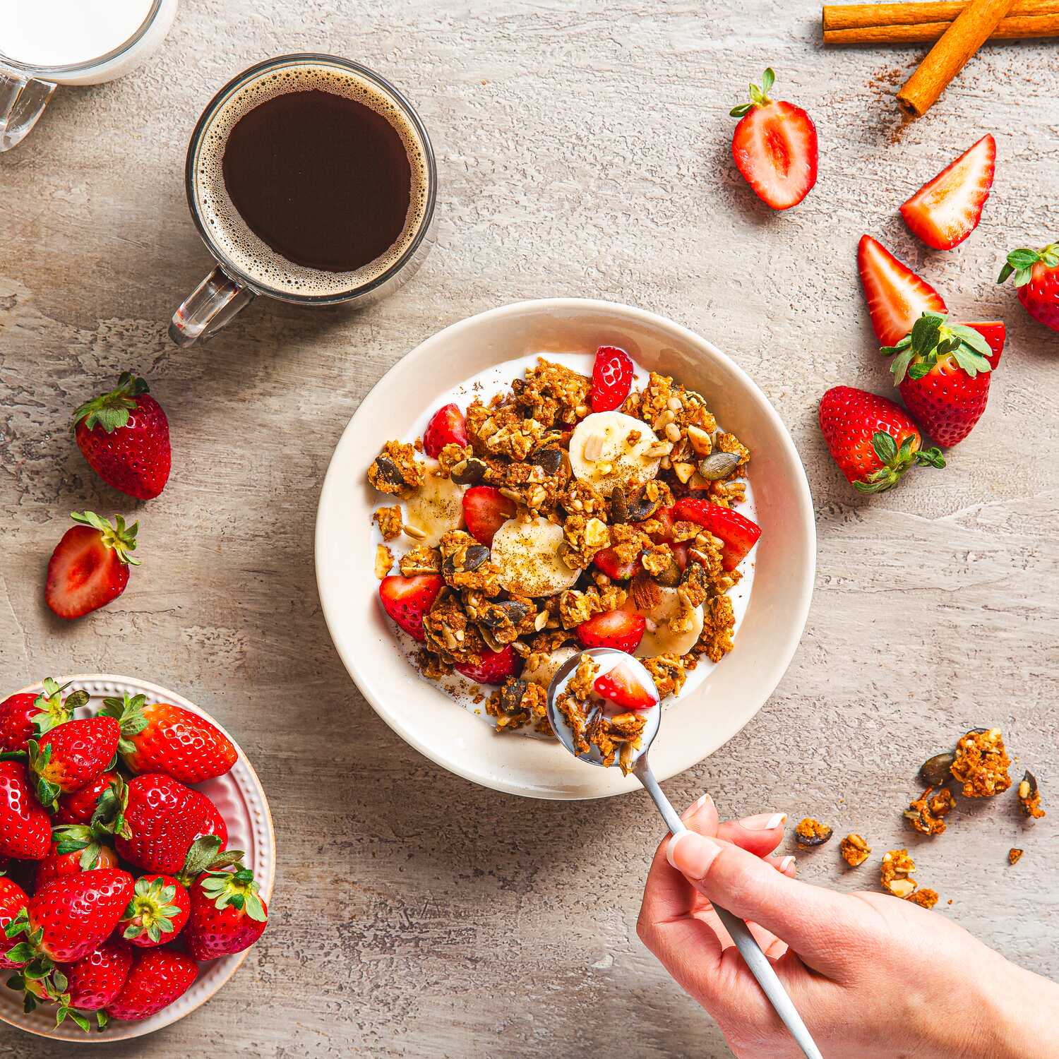 granola in cereal bowl with berries and coffee and hand