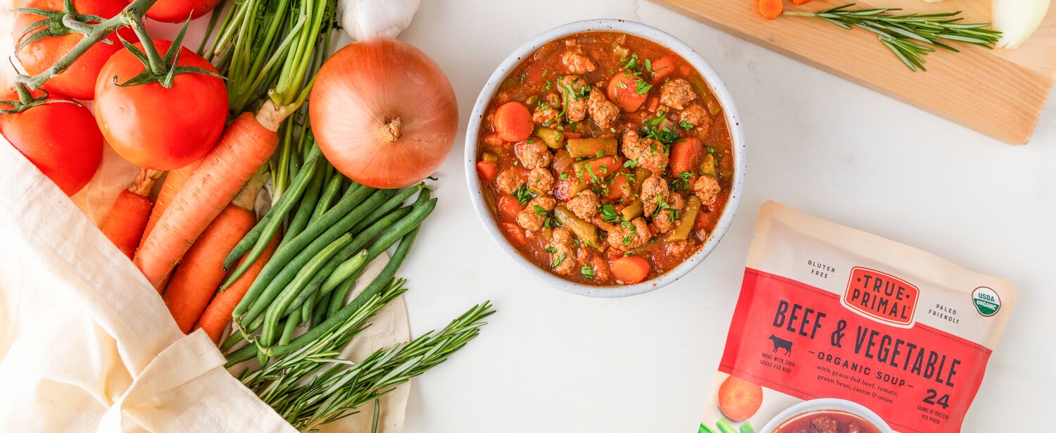 True Primal Beef & Vegetable Soup in bowl next to pouch and vegetables