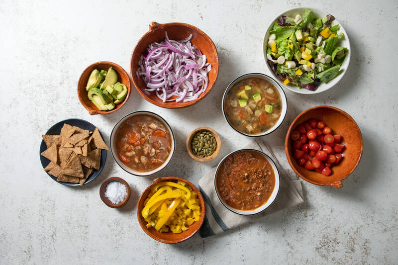 bowls of prepared food and ingredients with salad and soup and chili
