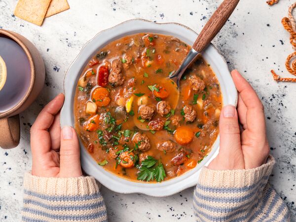 hands holding bowl of True Primal Hearty Beef Organic Soup next to candle and crackers