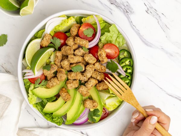 True Primal Grass-fed Beef Mini Meatballs on salad in bowl with hand and fork