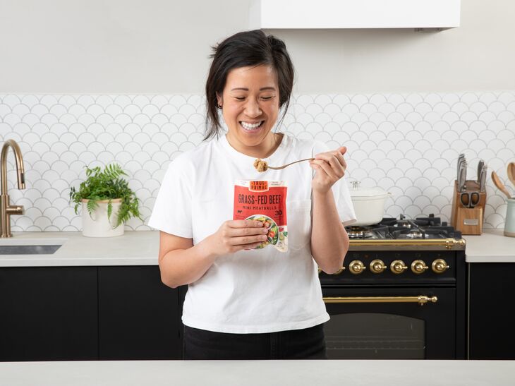 woman eating True Primal Grass-Fed Beef Mini Meatballs smiling and holding pouch