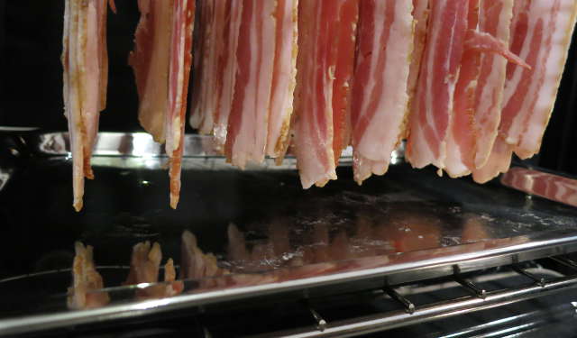 raw bacon hanging high enough to leave space above cookie sheet