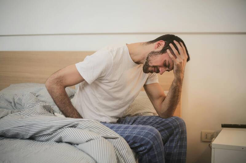 man sitting on bed holding head