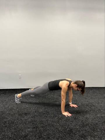 Woman in a high plank position. Hands under the shoulders with straight arms and legs straight back behind.