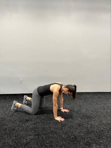 Woman in a quadruped position. Arms straight with hands under the shoulders, knees bent under the hips, knees and toes also on the ground.
