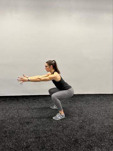 Woman in bottom position of a squat. Hips are knee hip, feet hip distance apart.