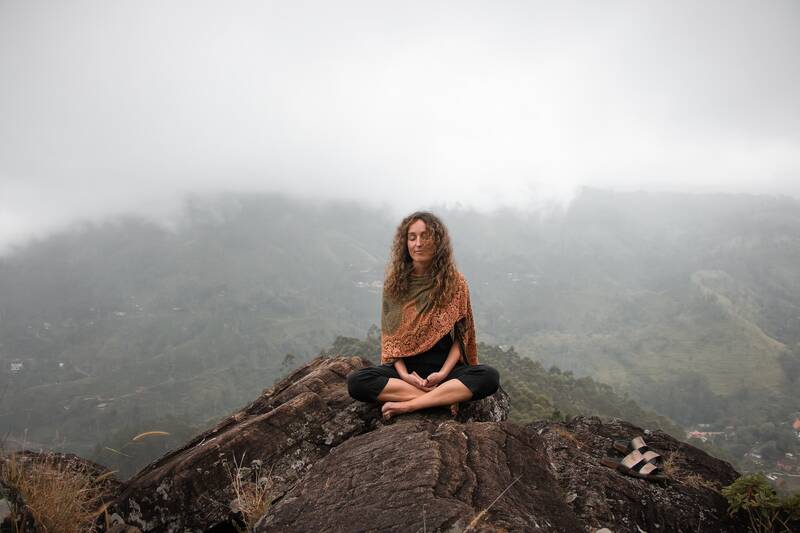 woman meditating on a hill top in a forest