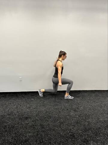 Woman performing a split squat with hand holding the wall for support.
