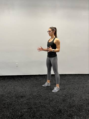 Woman standing ready to begin a squat, with feet hip distance apart.
